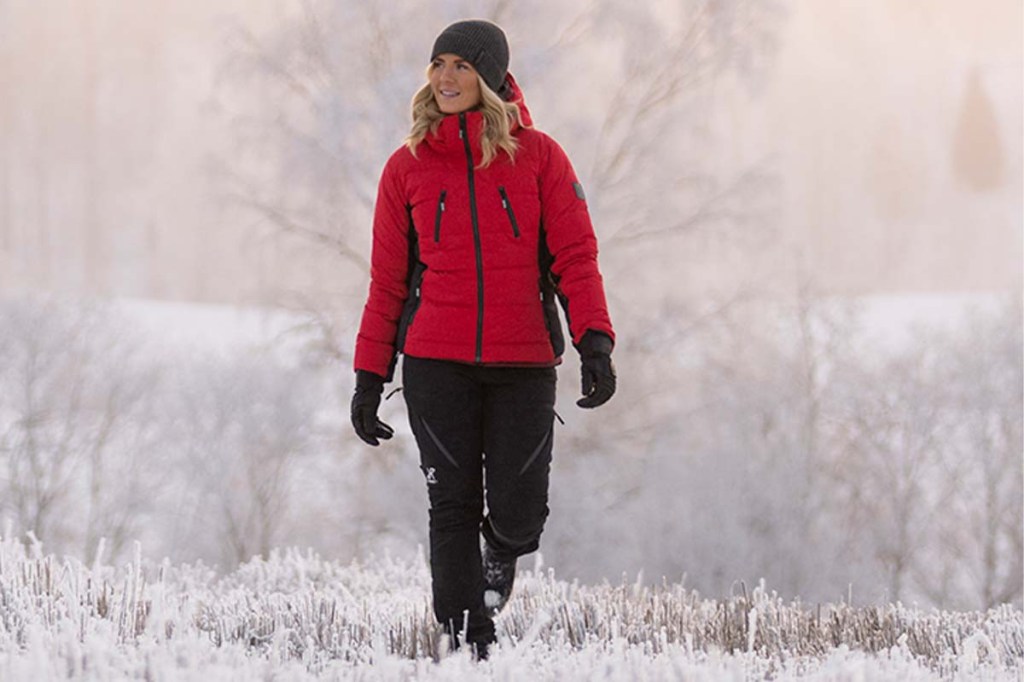 Frau mit roter Jacke und schwarzer Hose wandert durch eine winterliche Landschaft