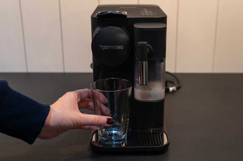 Ein Glas wird unter den Kaffee-Auslauf der De'Longhi Nespresso EN150 gestellt. Der Milchbehälter ist ebenfalls angebracht.