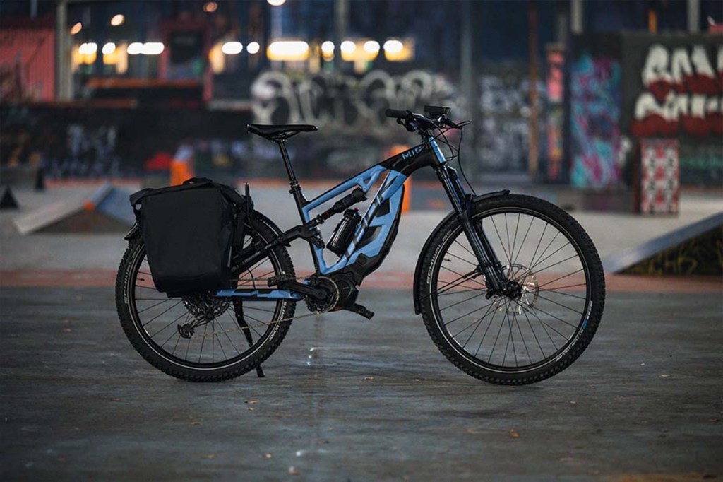 E-Bike mit Gepäcktaschen nachts auf einem Platz stehend, Beleuchtung im Hintergrund