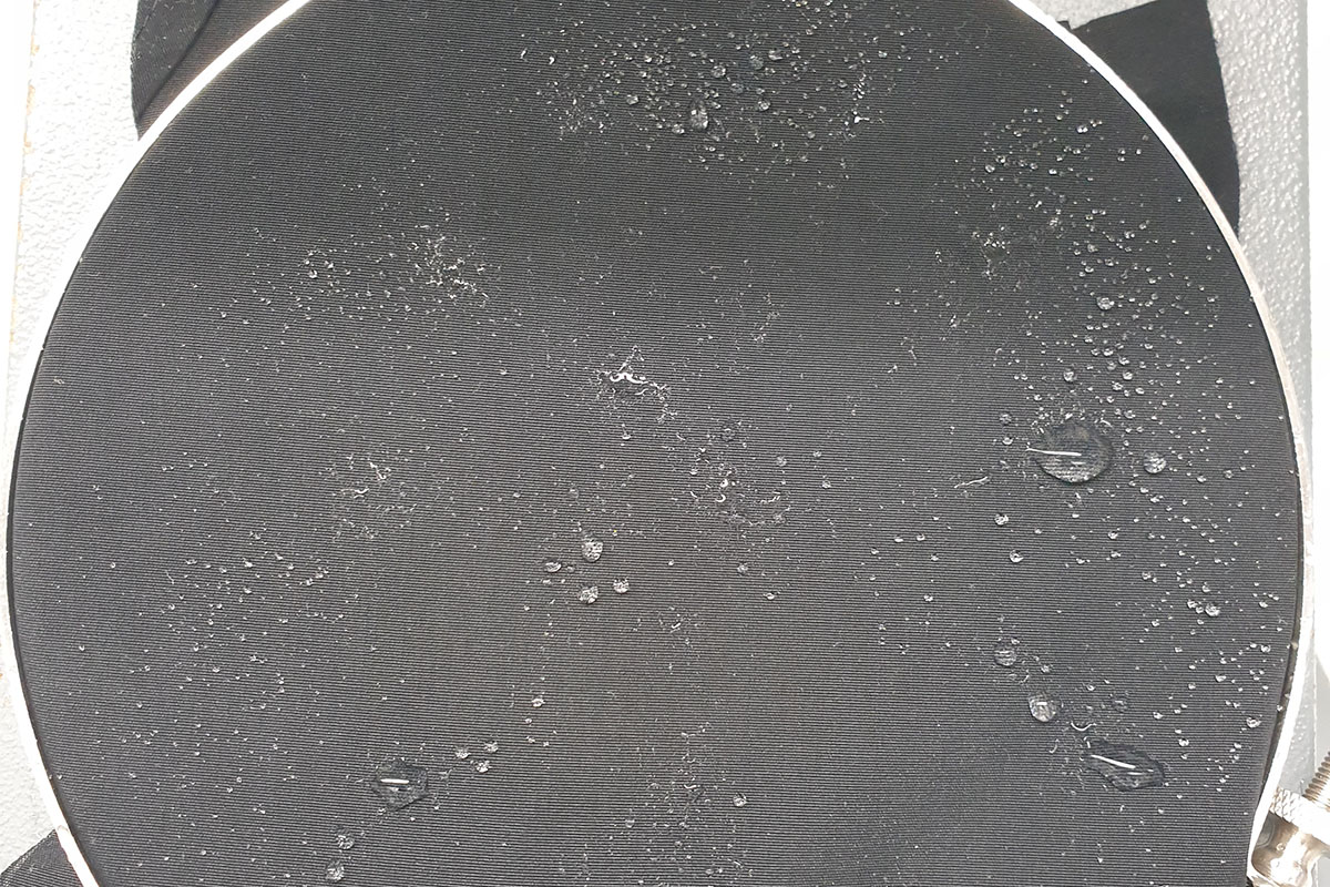 Detailaufnahme des Oberflächenstoffs bei einer Regenjacke mit Wassertropfen, die an der Oberfläche haften.
