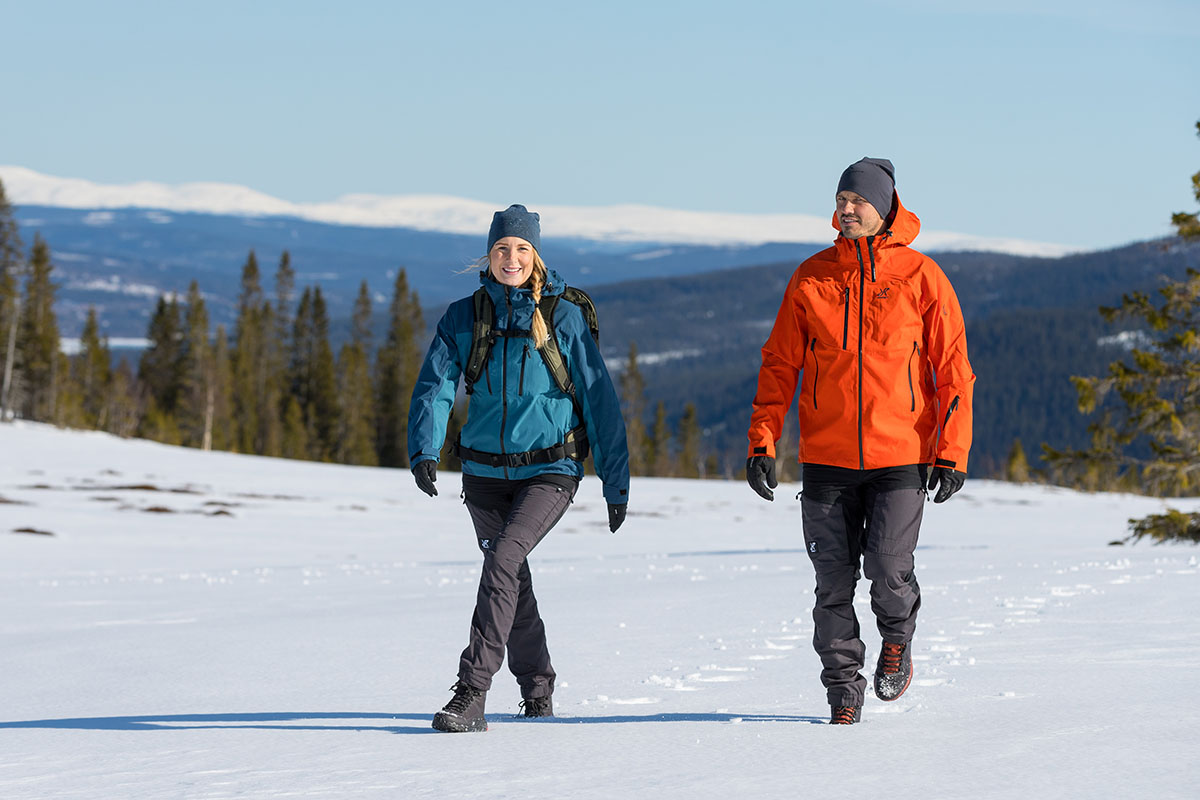 Frau und Mann mit Regenjacken bekleidet wandern durch Schneelandschaft im Gebirge.