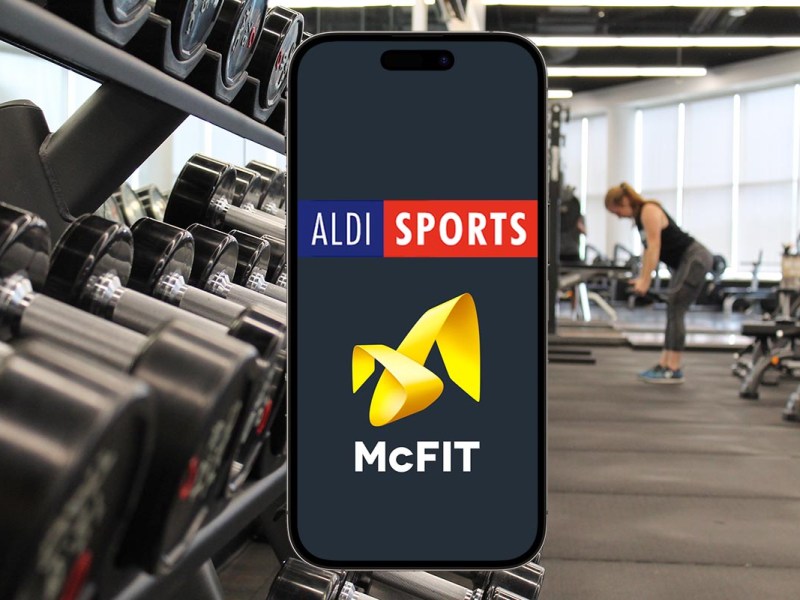 Fitnessstudio mit Regalen voller Hanteln. Im Hintergrund eine Frau.
