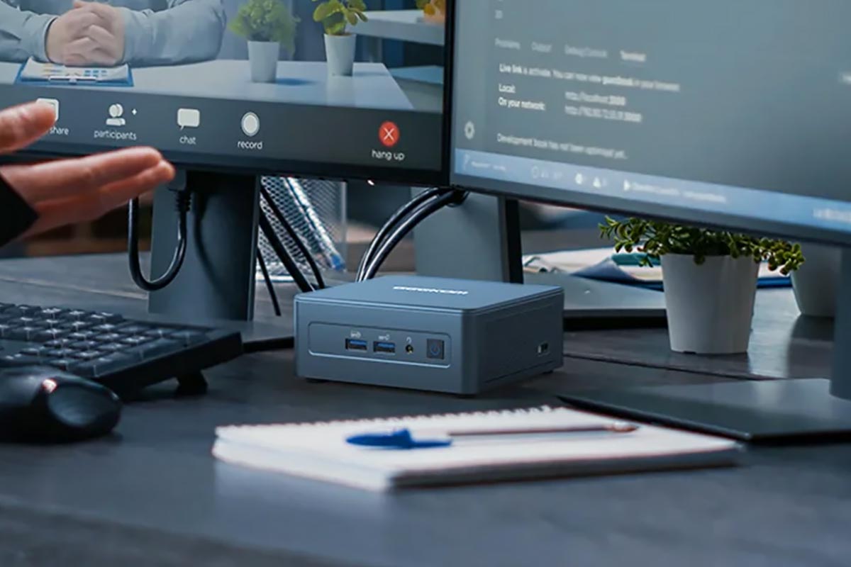 Mini-PC unter Monitoren auf einem Tisch.