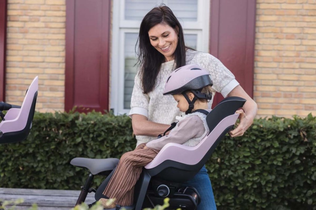 Frau steht hinter einem Fahrrad und stellt den Kindersitz passend ein, darin befindet sich sein Kind