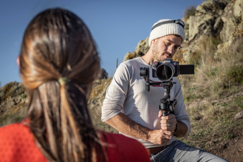 Man filmt Frau mit Kamera auf Gimbal vor Naturpark