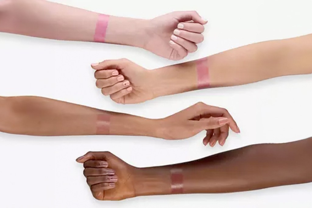 Mehrere Arme in unterschiedlichen Hautfarben liegen auf einem weißen Untergrund. Jeder trägt einen Lippenstift-Streifen wie ein Armband.