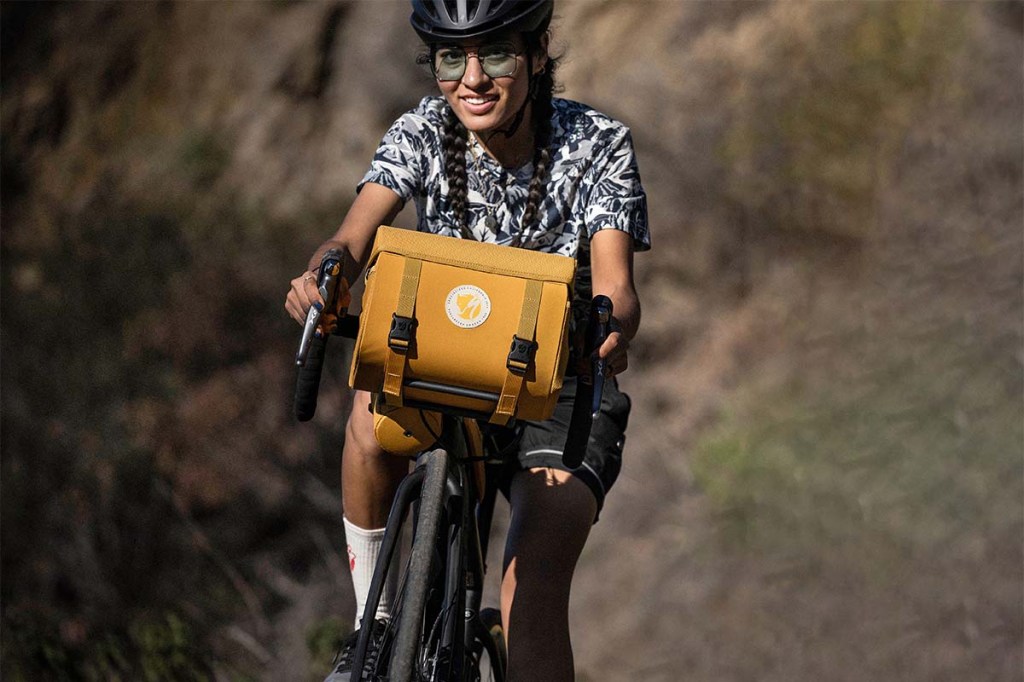 Frau fährt mit einem Fahrrad durch die Natur, am Lenker ist eine Tasche befestigt