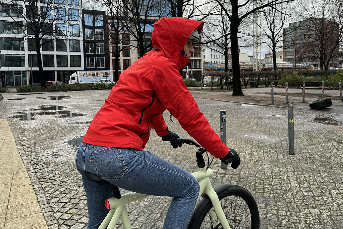 Frau mit Regenjacke auf E-Bike auf Marktplatz.