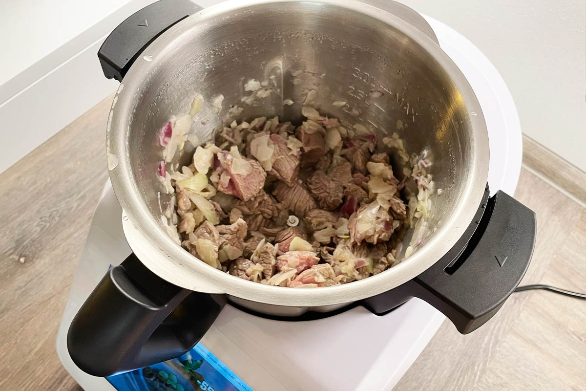 Geschnittene Zwiebeln und Knoblauchzehen sowie angebratenes Flesich im Mixtopf des Monsieur Cuisine Smart.