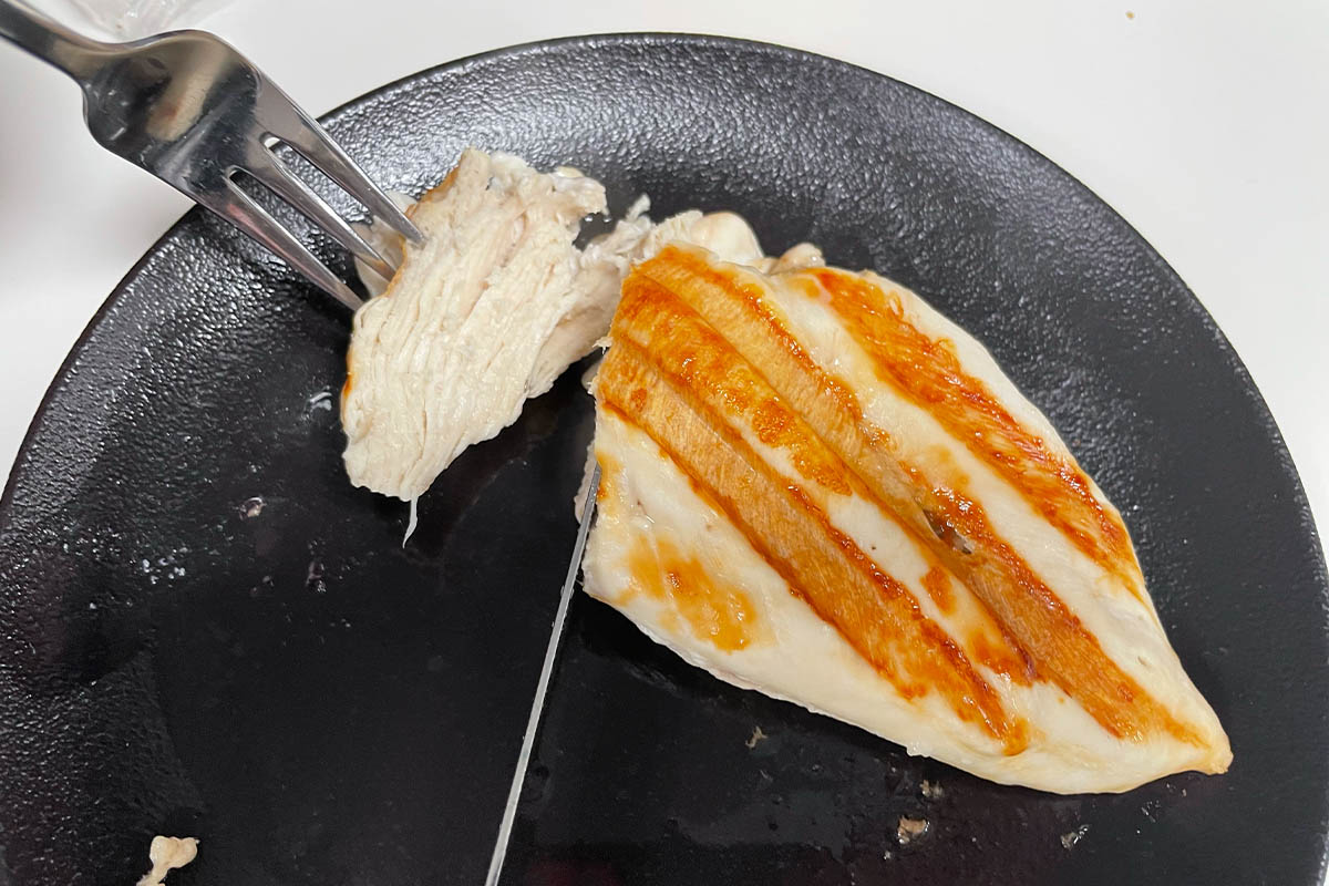 Ein gegrilltes Geflügelbrust-Filet wird auf einem dunklen Teller angeschnitten.