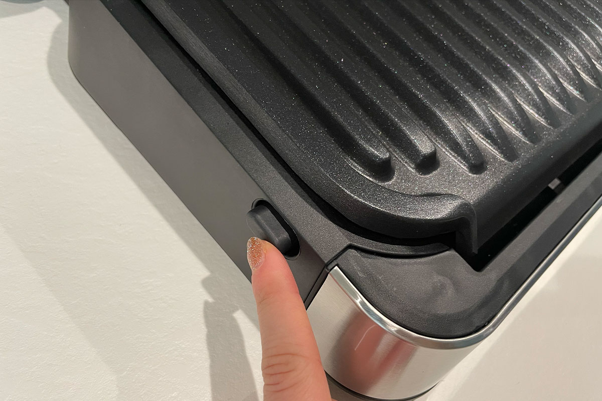 Ein Finger betätigt den seitlichen Knopf des Tefal-Kontaktgrills.