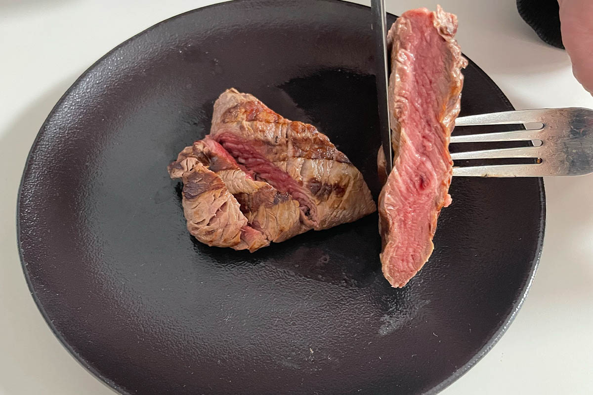 Ein gegrilltes Filet-Steak wird auf einem dunklen Teller angeschnitten.