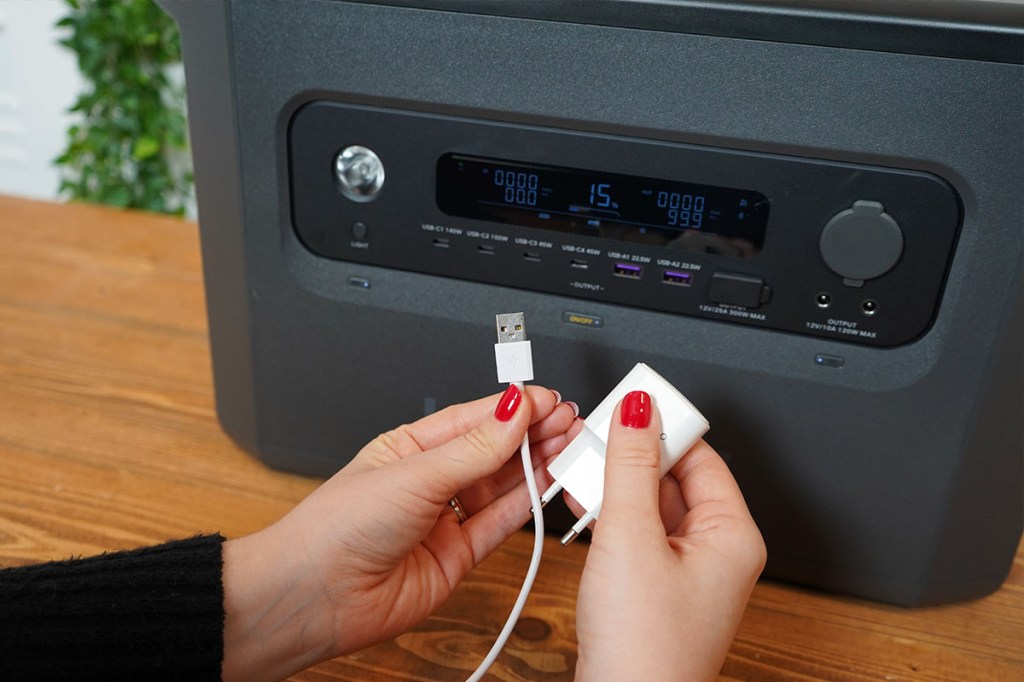 Eine Person hält ein Ladekabel und ein Netzteil vor die Ugreen-Powerstation.