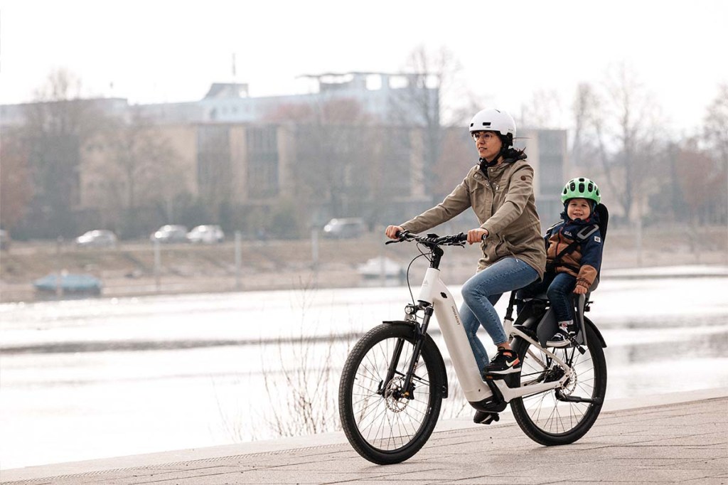 Frau fährt mit einem E-Bike, sie hat ein Kind auf einem Kindersitz dabei