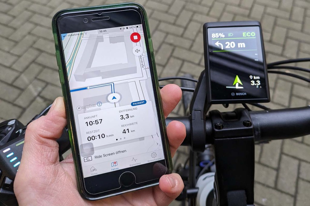 Display von Fahrrad, daneben hält eine Hand ein Smartphone fest