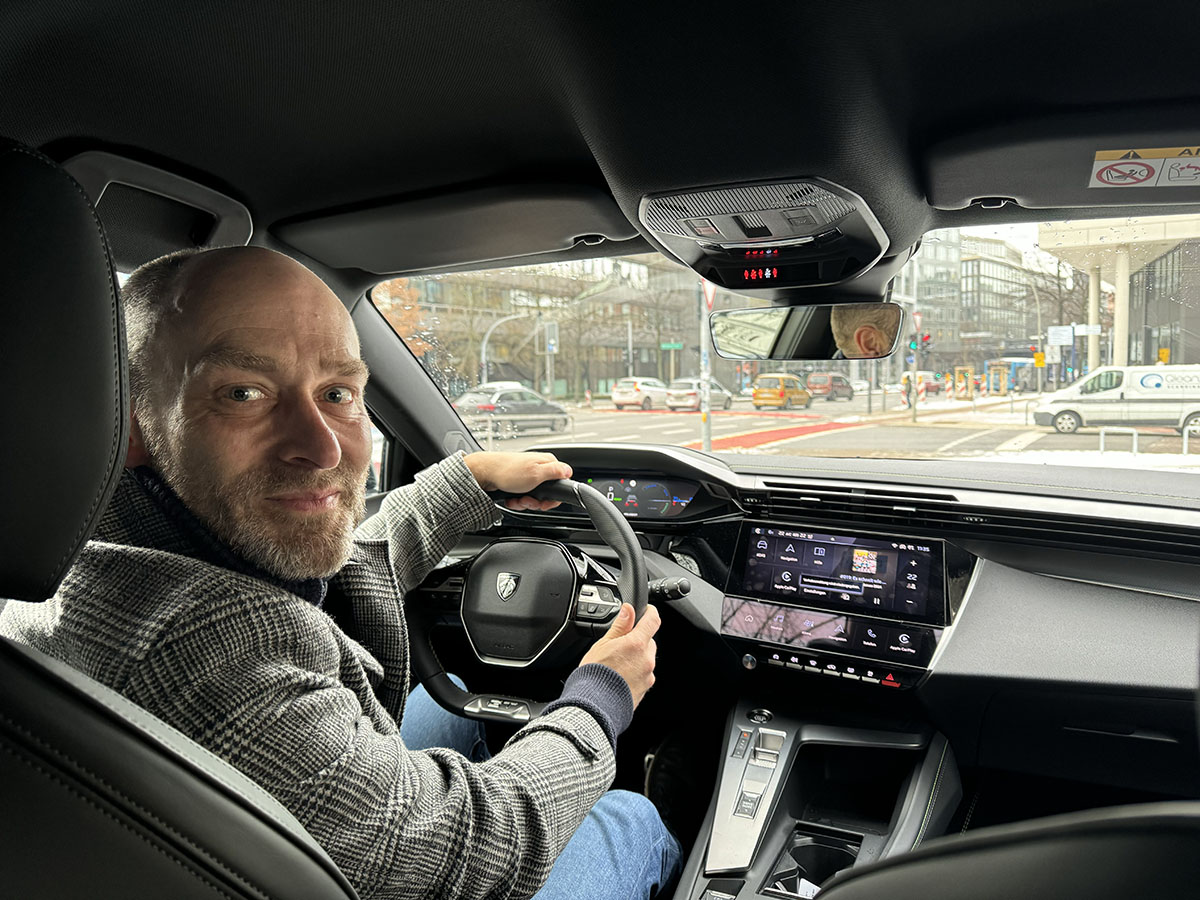 Lächelnder Mann in E-Auto mit Schulterblick auf die Rückbank.