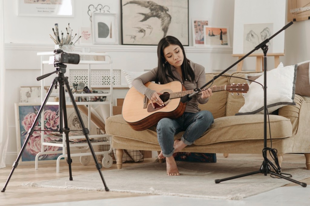 Frau spielt Gitarre und filmt sich dabei mit Systemkamera auf Stativ