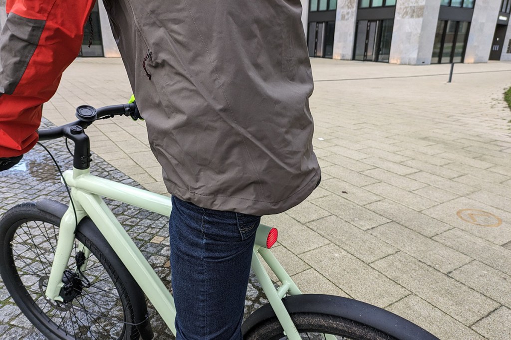 Fahrradfahrer in Rückansicht auf E-Bike trägt eine Regenjacke.