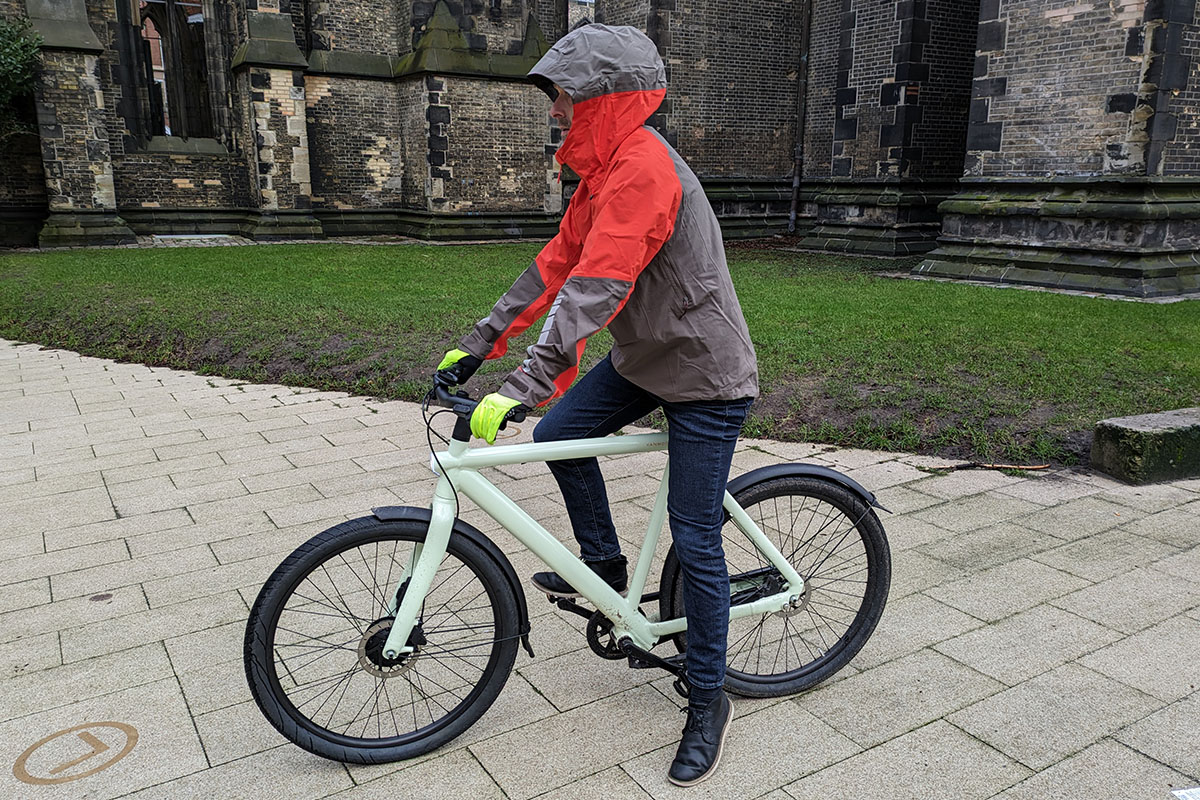 Mann auf E-Bike Mit Regenjacken, deren Kapuze über einen Fahrradhelm gezogen ist.