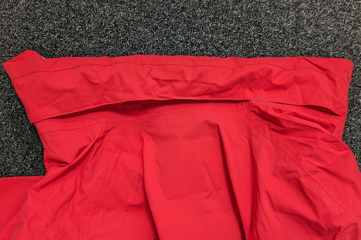 Detailaufnahme von einer Regenjacke, die mit eingerollter Kapuze auf einem Teppichboden liegt.