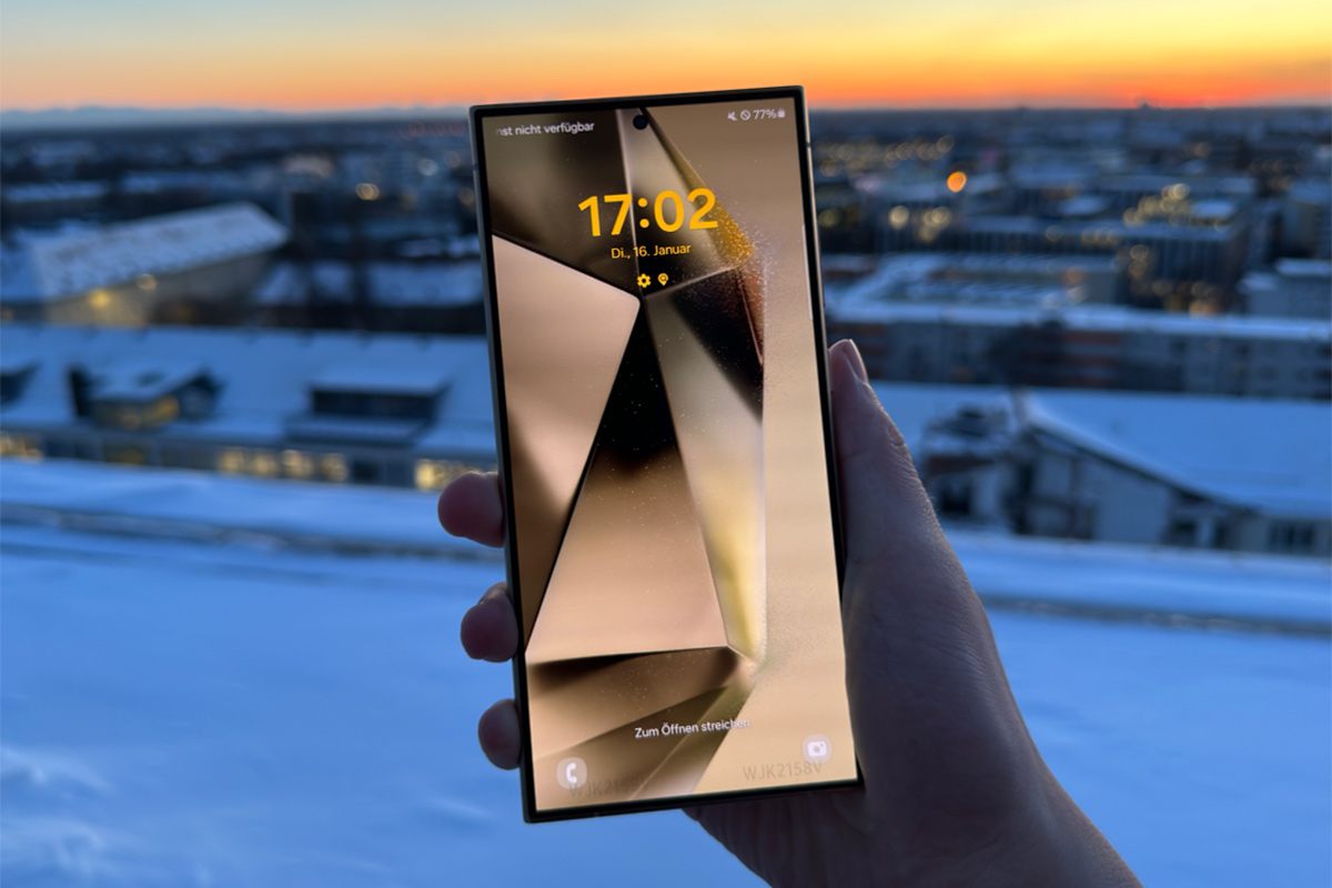 Das Smartphone Samsung Galaxy S24, in der Hand gehalten, vor einem Sonnenuntergang-Hintergrund.