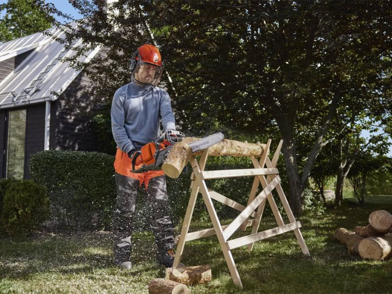 Ein Mann steht mit einer Kettensäge beim Brennholzsägen.