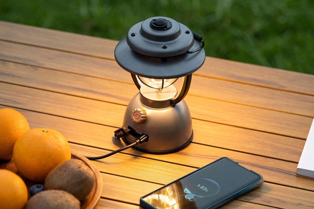 Camping-Laterne von OLight auf einem Holztisch neben Obst und einem Smartphone.