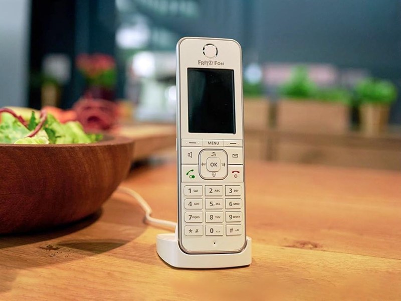 Festnetztelefon auf einem Holztisch neben einer Salatschale.