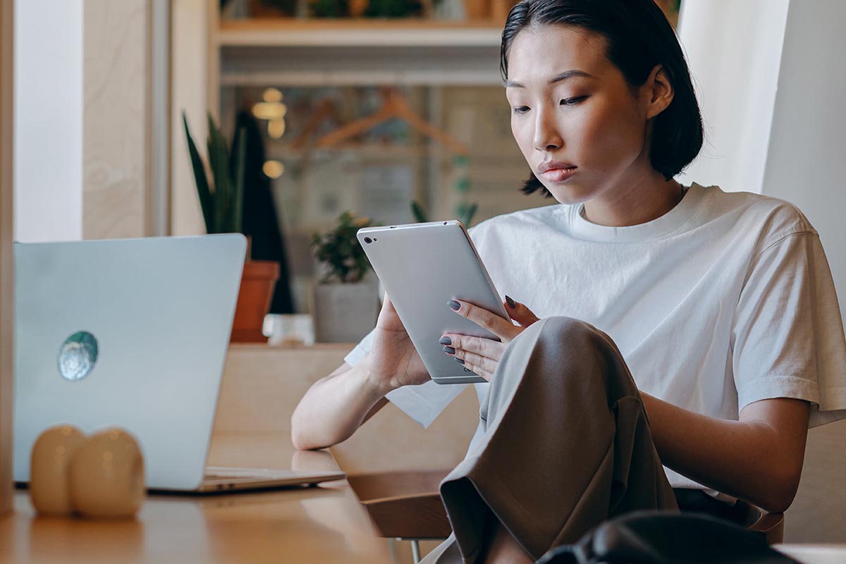 Person mit Tablet und Laptop an einem Tisch sitzend.