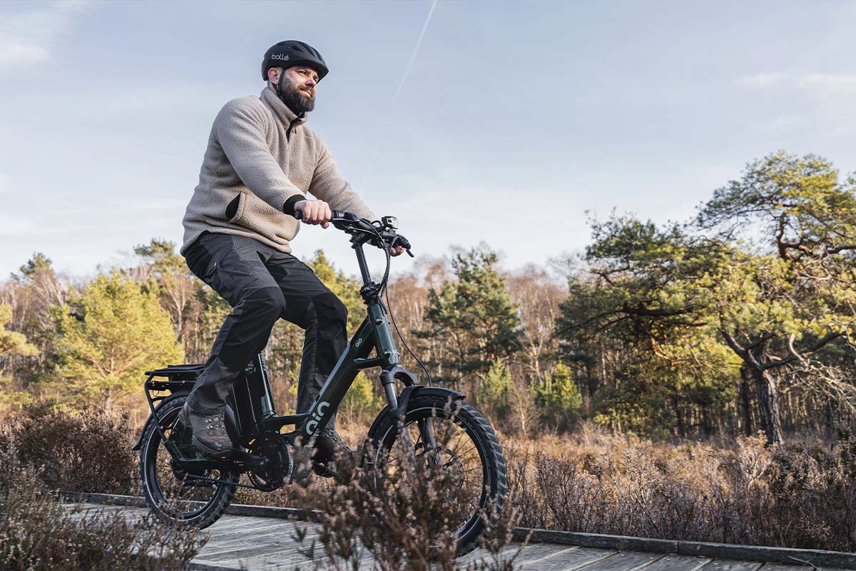 Mann fährt mit einem Kompakt-E-Bike über einen Holzsteg, der durch eine Waldlandschaft führt