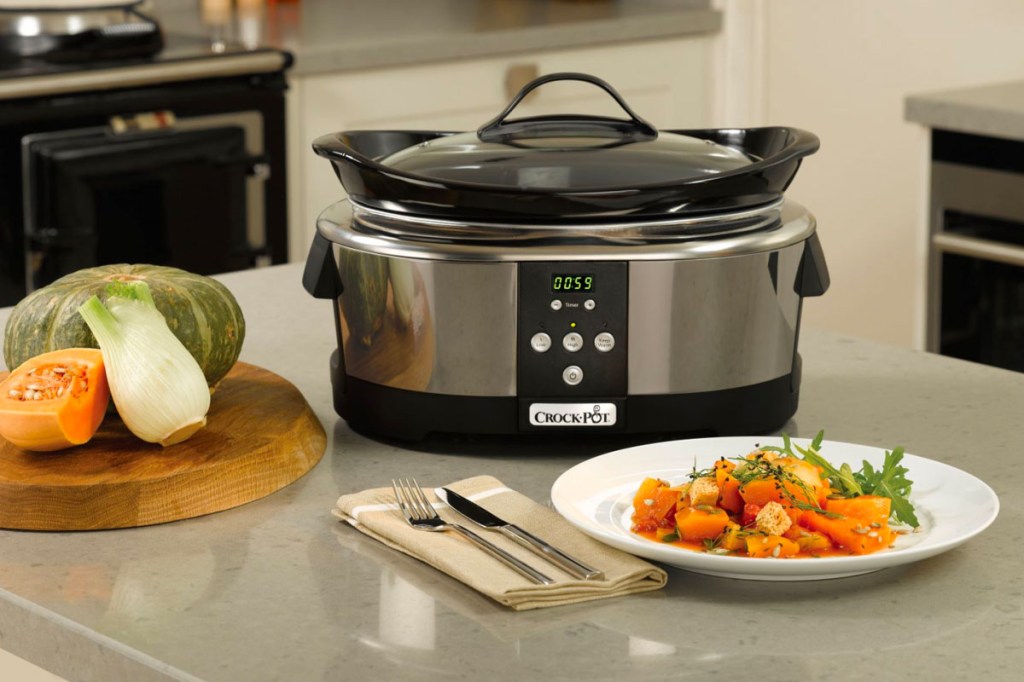 Der Slow Cooker von Crock-Pot steht auf einer Arbeitsfläche einer Küche mit verschiedenen Gerichten drum herum.
