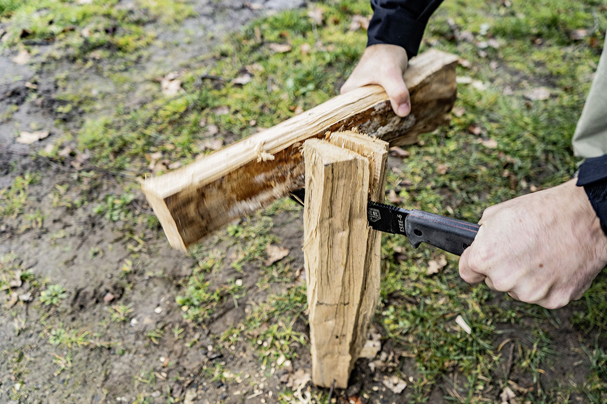 Outdoormesser wird zum Spalten eines Holzscheites genutzt. Dafür wird mit einem weiteren Holzstück auf die Klinge des MNesser geschlagen, um diese durch den Holzscheit zu treiben.