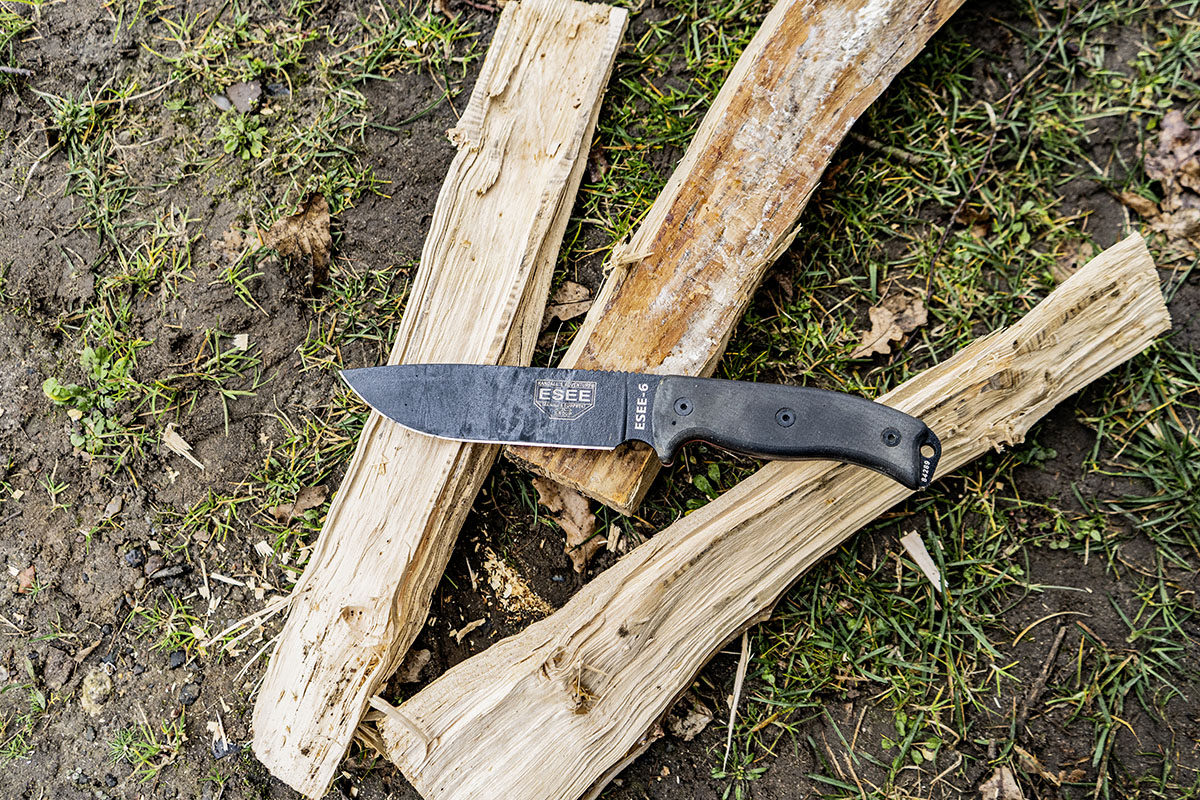 Outdoormesser liegt auf drei gespaltenen Holzscheiten auf Rasenfläche.