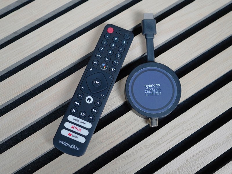 Der Freenet TV Hybrid TV Stick liegt auf einer Holzoberfläche neben der Fernbedienung.