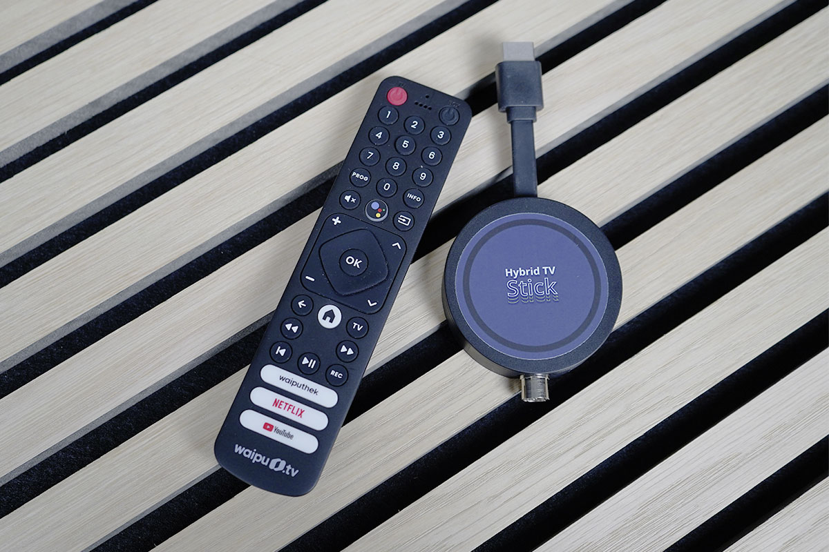 Der Freenet TV Hybrid TV Stick liegt auf einer Holzoberfläche neben der Fernbedienung.