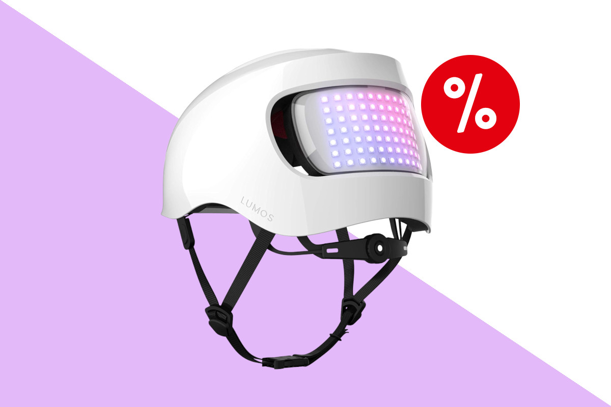 Weißer Lumos-Fahrradhelm schräg von hinten mit schwarzem hängenden geschlossenen Riemen und lila rosa leuchtender LED-Fläche auf lila weißem Hintergrund mit rotem Prozentbutton oben rechts