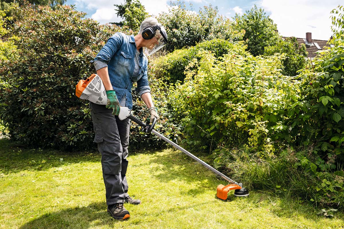 Ein Person arbeitet mit einem Rasentrimmer im Garten.