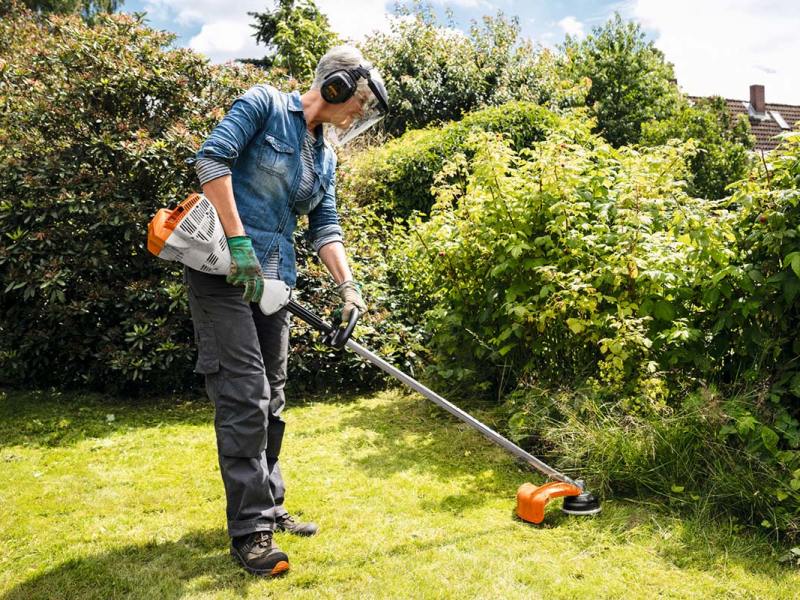 Ein Person arbeitet mit einem Rasentrimmer im Garten.