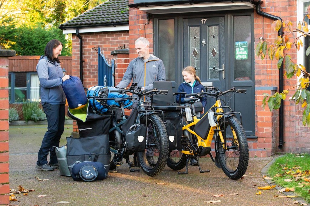 Drei Personen stehen neben ihren vollbelanden E-bikes vor einem Haus