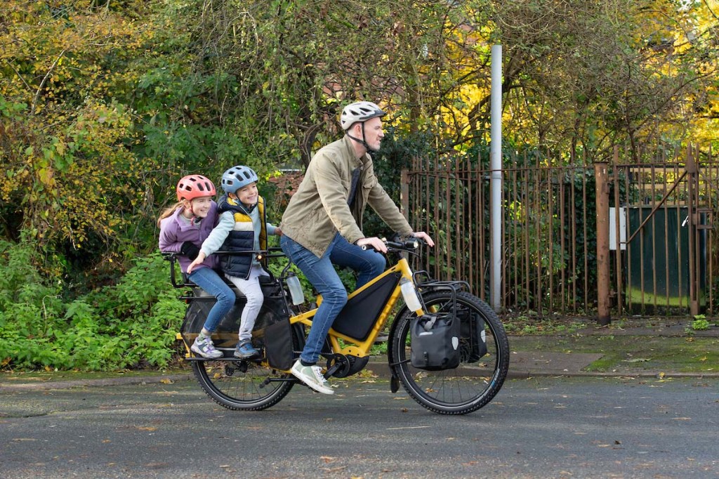 Mann fährt auf einem E-Bike, auf dem Gepäckträger sitzen zwei Kinder