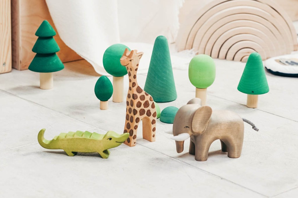 Eine Holzgiraffe, ein Holzkrokodil und ein Holzelefant stehen vor Holzbäumen