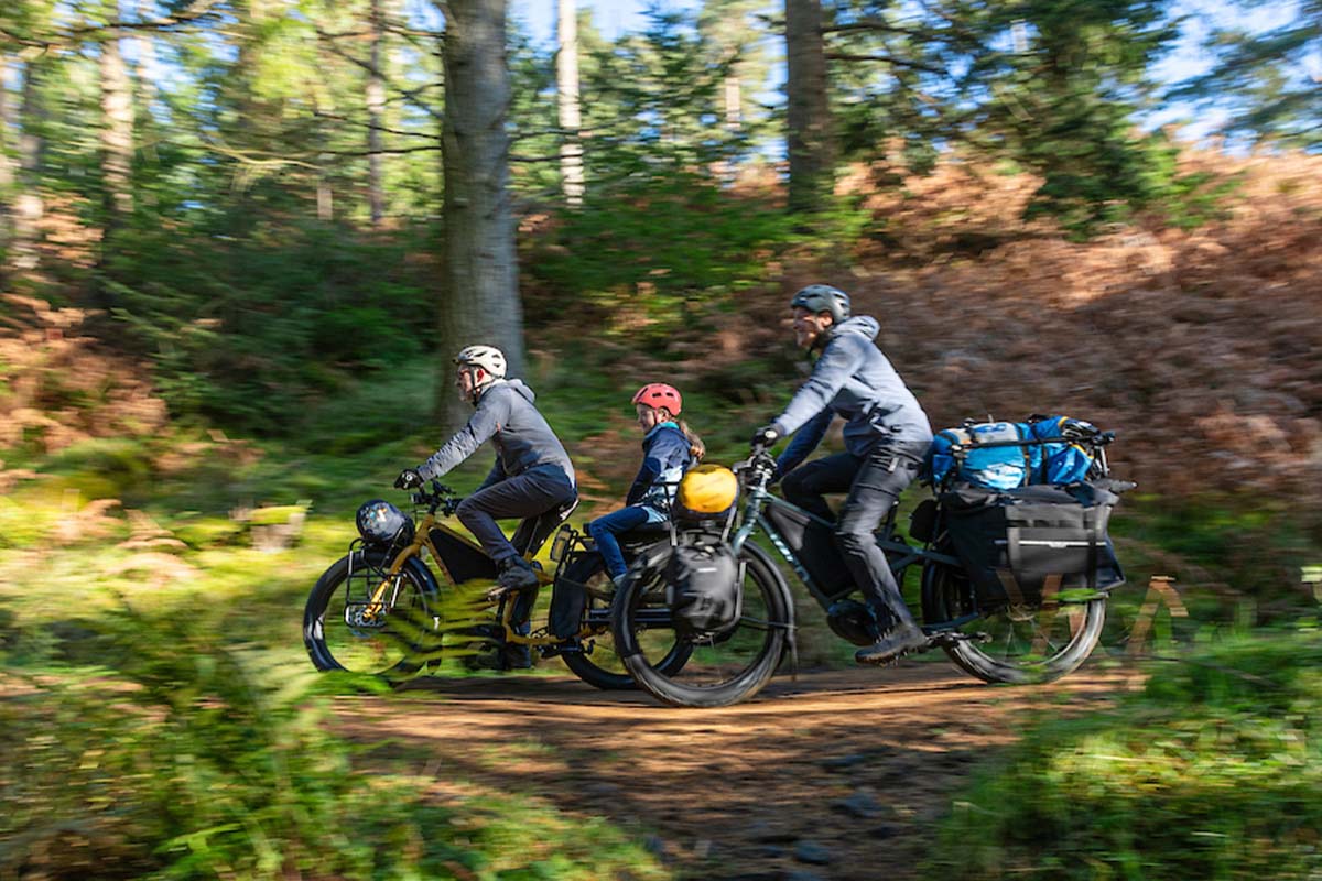 Familie fährt auf vollbeladenen Fahrrädern durch einen Wald
