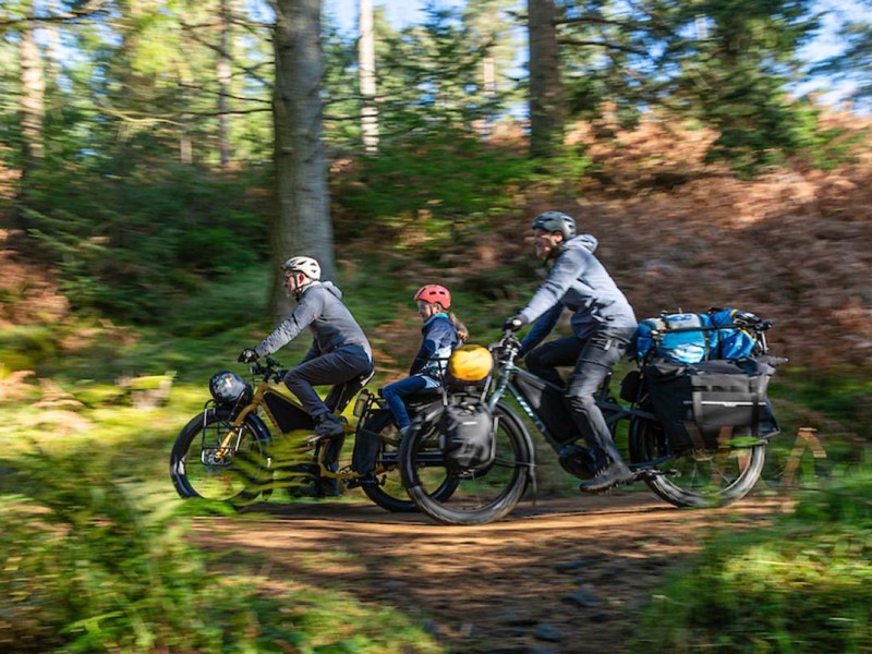 Familie fährt auf vollbeladenen Fahrrädern durch einen Wald