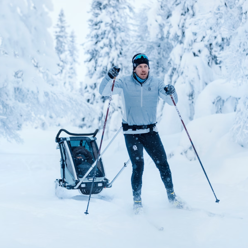Ein Mann zieht beim Skilanglauf einen Fahrradanhänger mit einem Kinder durch eine verschneite Gegend.
