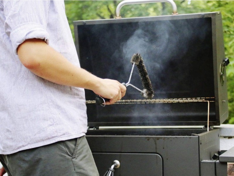 Person mit Zubehör für einen Grill in der Hand.