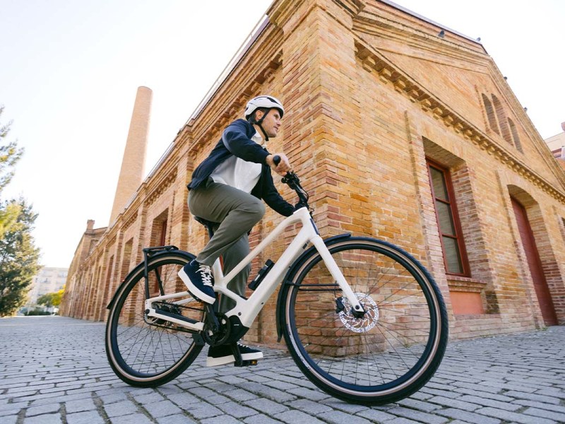 Fahrradfahrer fährt mit einem E-Bike, im Hintergrund ein Backsteingebäude
