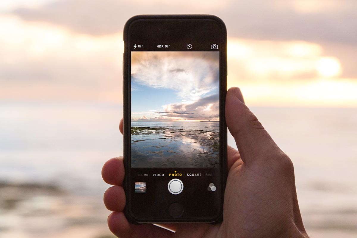 In der Hand gehaltenes iPhone, mit dem ein Foto vom Meer geschossen wird.