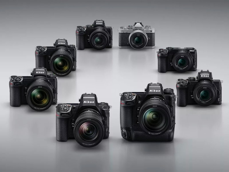 8 Nikon-Kameras vor silbergrauem Hintergrund.