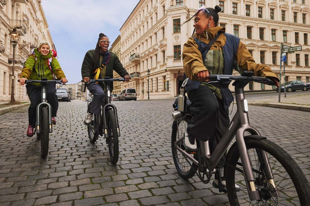 Drei Personen fahren mit einem E-Bike durch eine Stadt