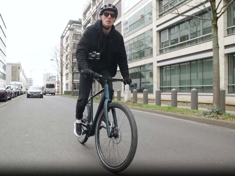 Mann fährt mit einem Rad durch die Stadt, man sieht in von vorne auf die Kamera zufahren